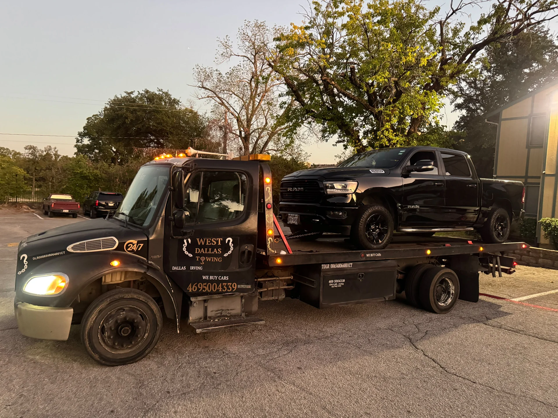 West Dallas Towing flatbed carrying RAM 1500 truck at dusk with marker lights in Dallas